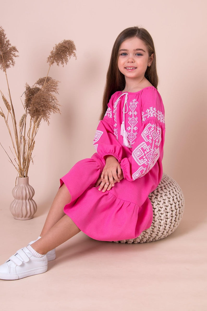 Girl wearing pink embroidered vyshyvanka dress with Ukrainian folk patterns. Linen-viscose material, perfect for cultural events.