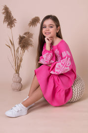 Girl wearing pink embroidered vyshyvanka dress with traditional Ukrainian patterns, sitting in a stylish setting.