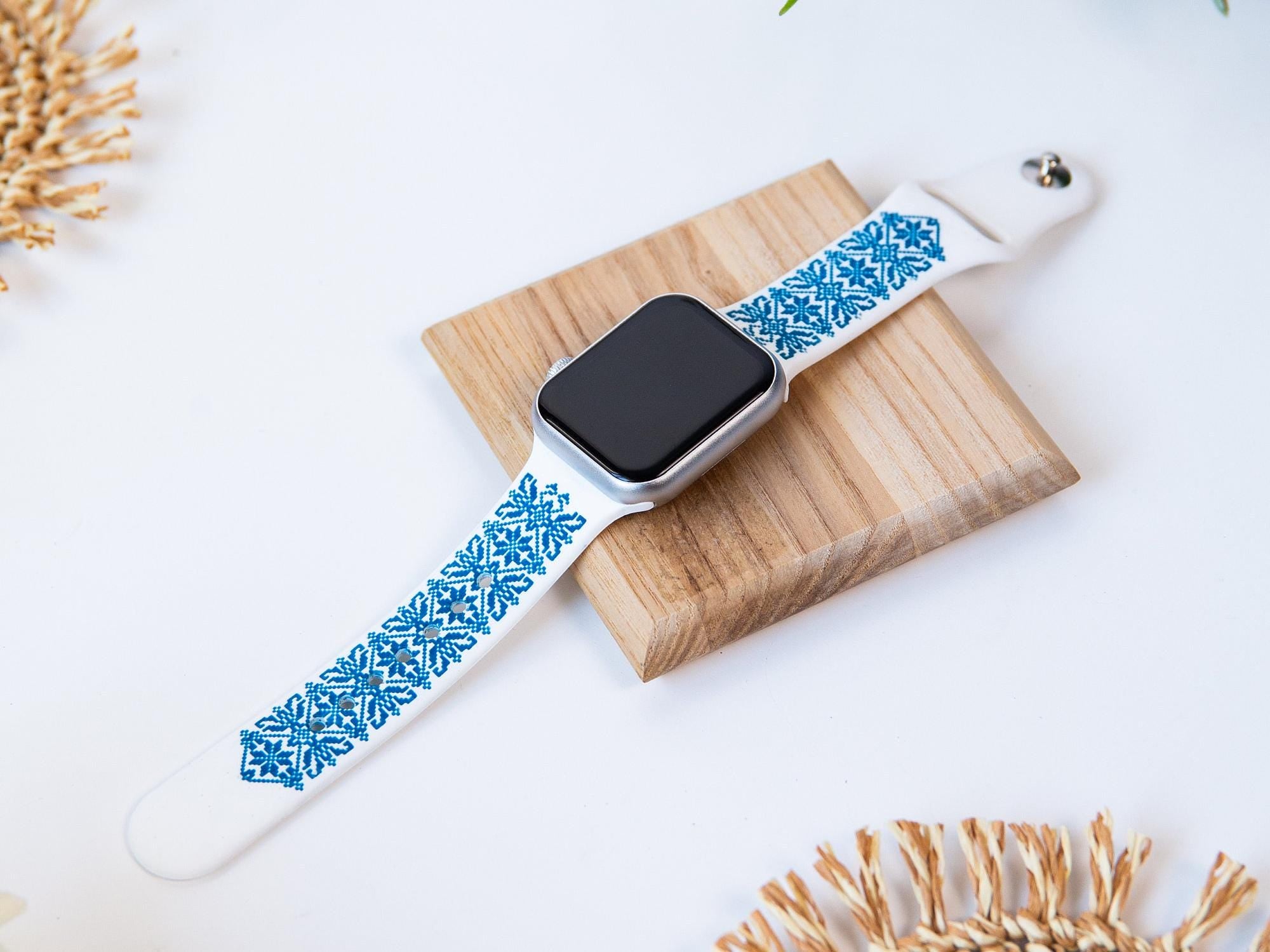 White and blue silicone Apple Watch band with engraved Ukrainian embroidery on wooden stand