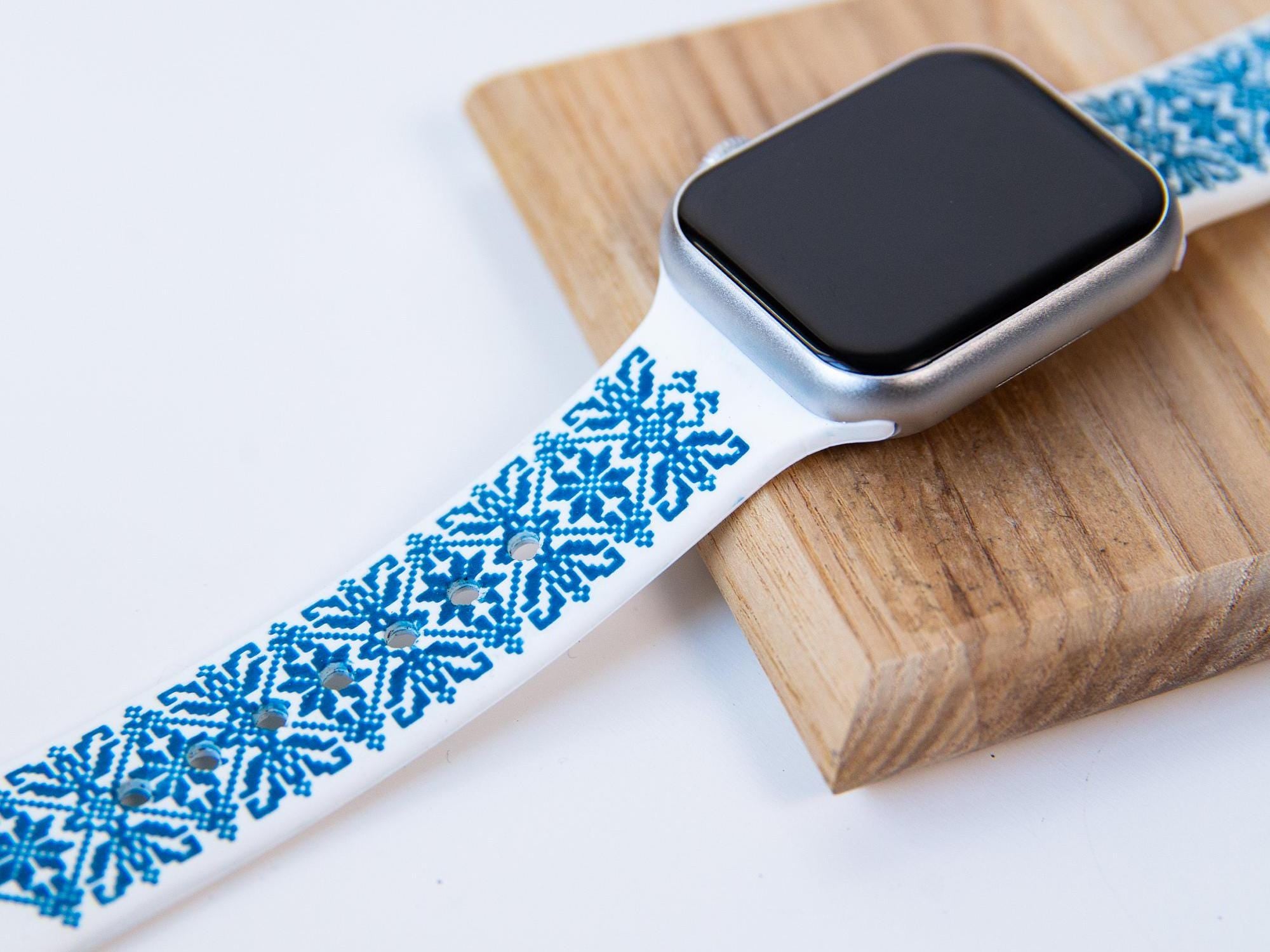 White and blue Ukrainian embroidery Apple Watch band, silicone strap, on wooden background, showcasing intricate design.