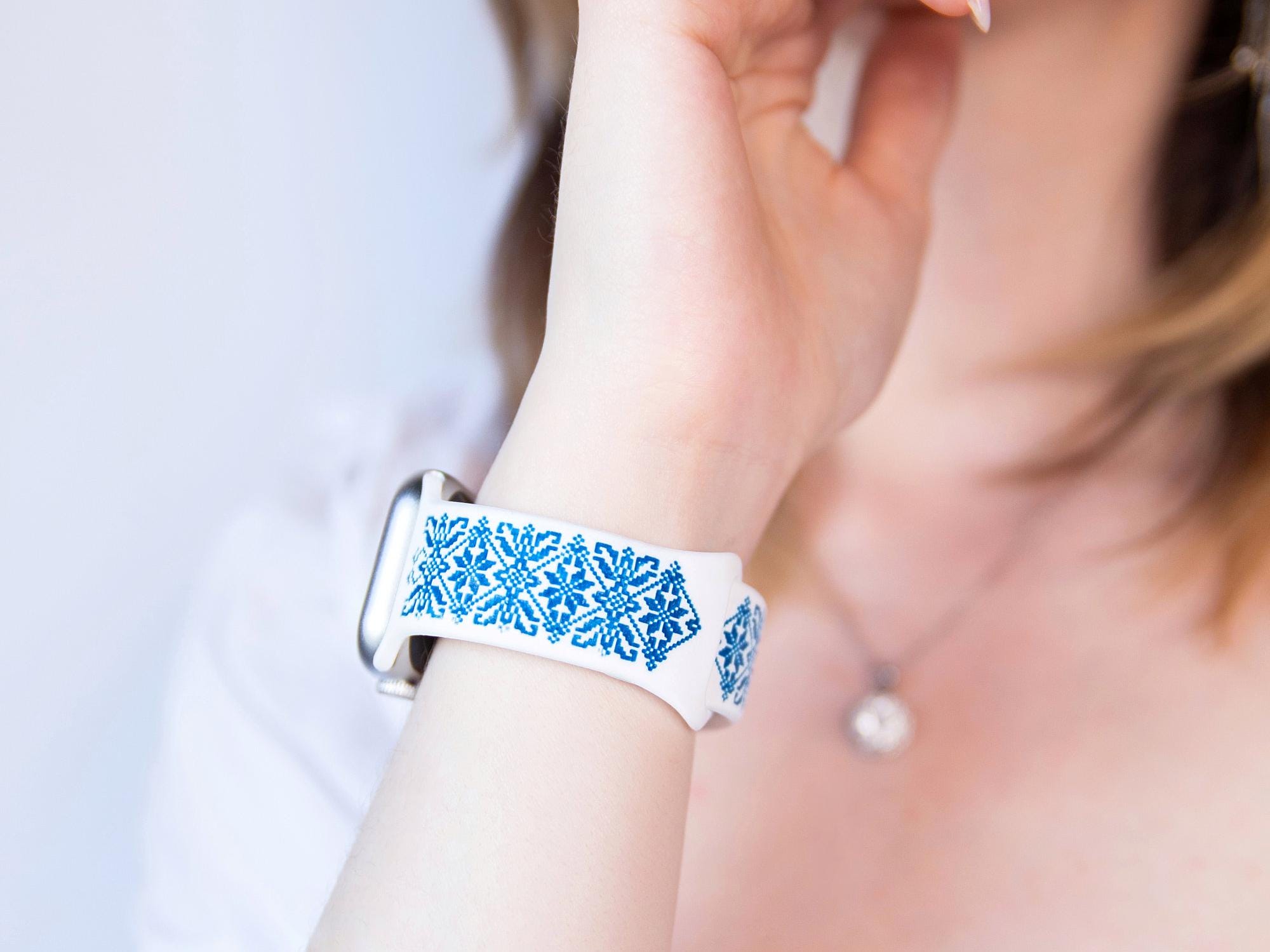 Elegant Ukrainian embroidery Apple Watch band in white and blue silicone, showcasing intricate traditional patterns on a wrist.