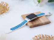 Elegant white and blue Apple Watch band with Ukrainian embroidery design, displayed on a wooden platform.