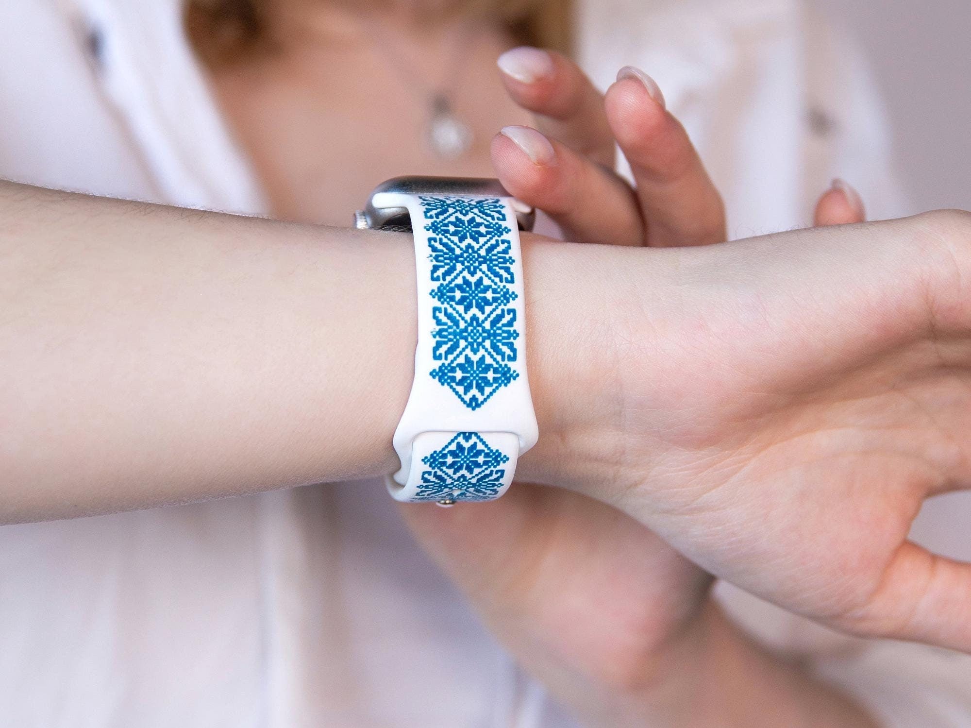 White and blue silicone Apple Watch band with Ukrainian embroidery design, worn on wrist, showcasing intricate engraving.