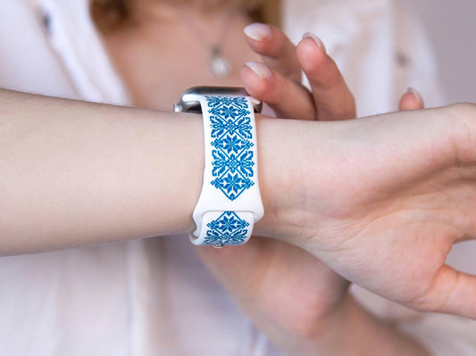 White and blue silicone Apple Watch band with Ukrainian embroidery design, worn on wrist, showcasing intricate engraving.