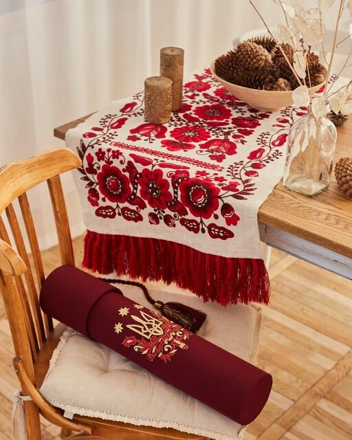 Ukrainian embroidered wedding rushnyk on table, featuring red cross-stitched motifs on natural linen, symbolizing protection and blessings.