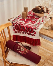 Ukrainian wedding rushnyk embroidered with red traditional symbols, draped over a chair next to a linen cushion.