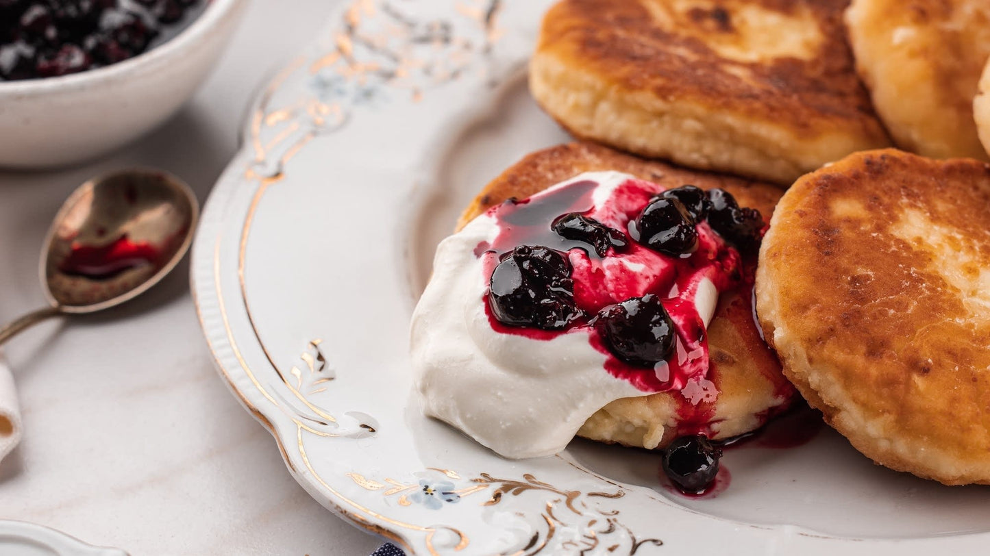 Authentic Ukrainian syrnyky pancakes served with cream and berry topping on an elegant plate. Perfect for breakfast or dessert.