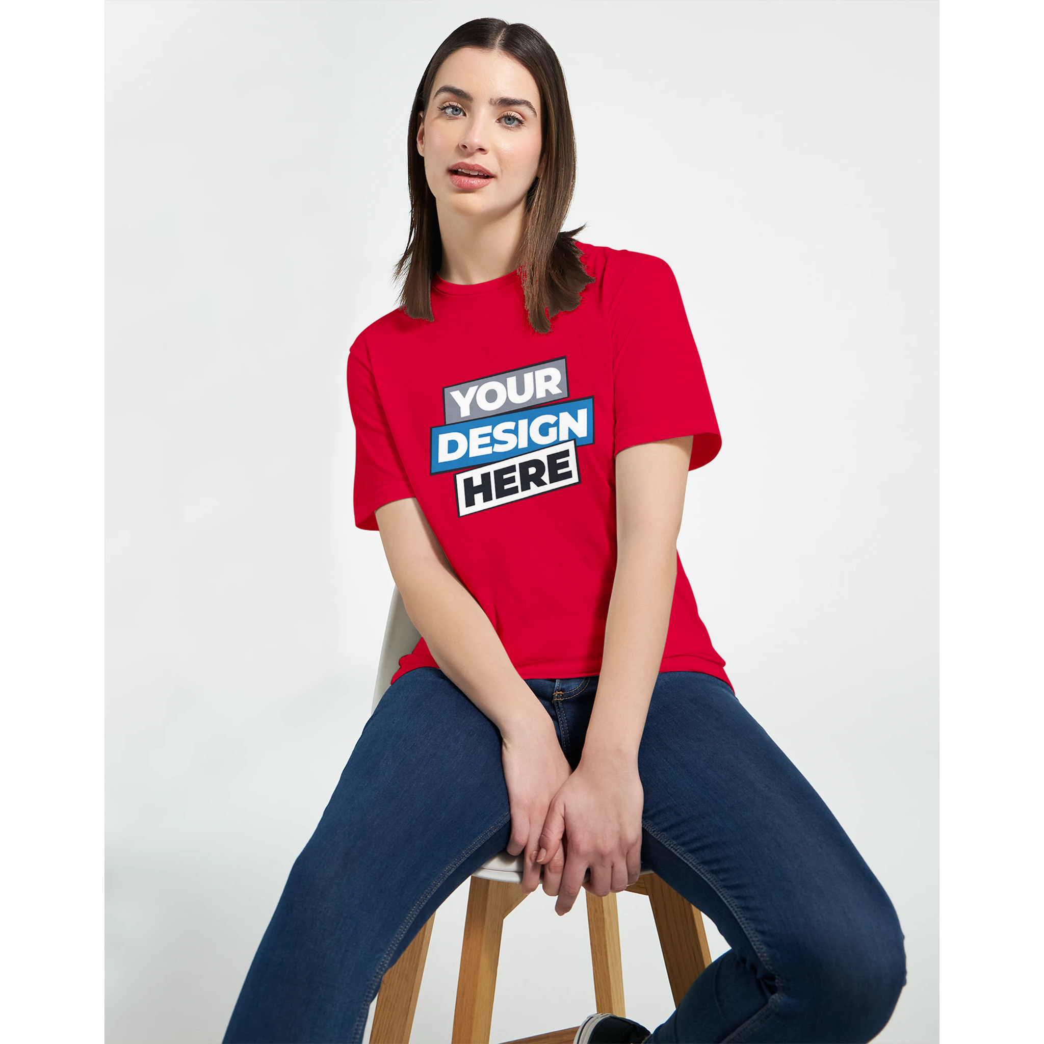 Woman wearing a red print-on-demand t-shirt with text 'Your Design Here', sitting on a stool, showcasing custom apparel options.