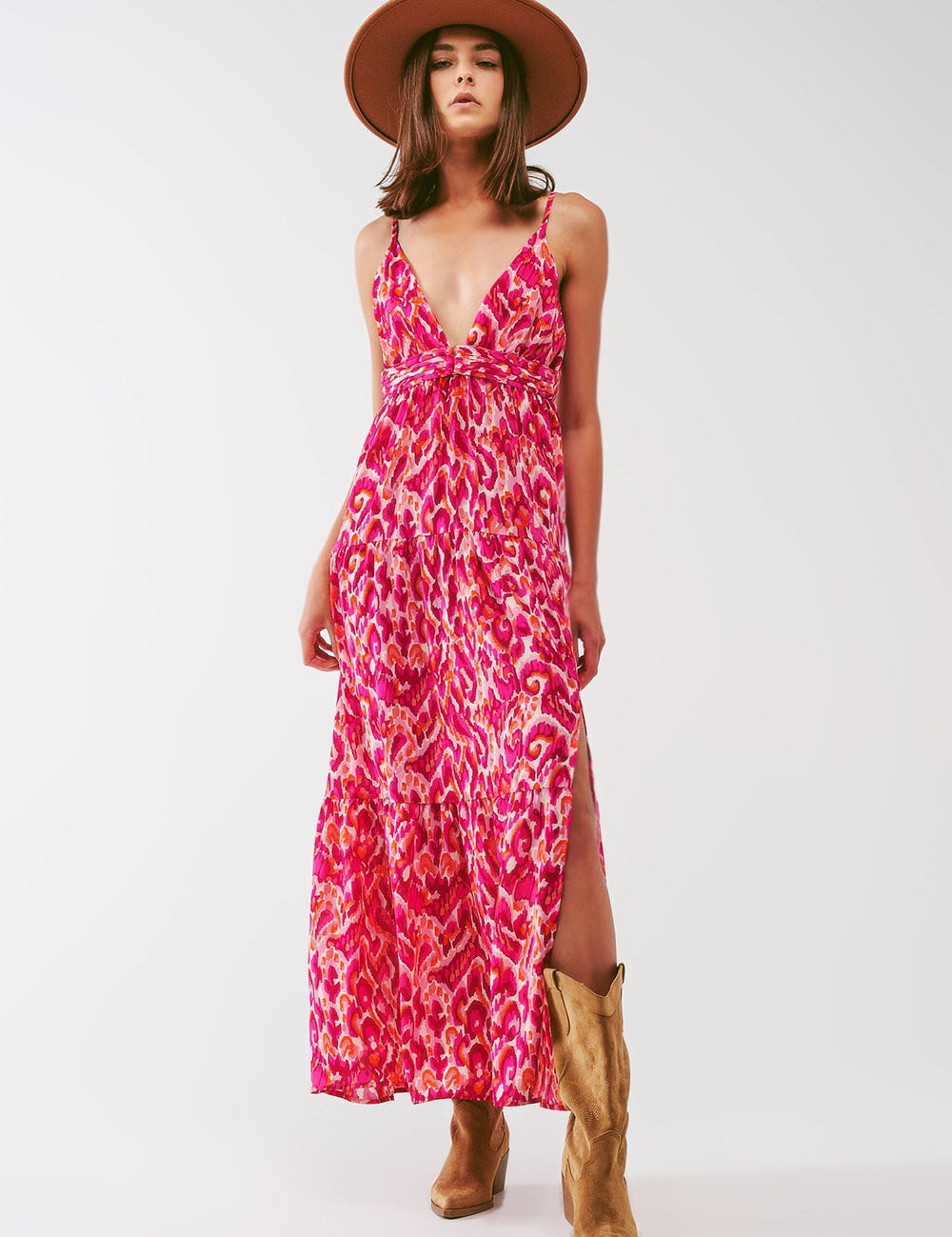 Woman in Floralia Pink Maxi Dress with floral pattern, wide V-neckline, and sleeveless design. Paired with a hat and cowboy boots.