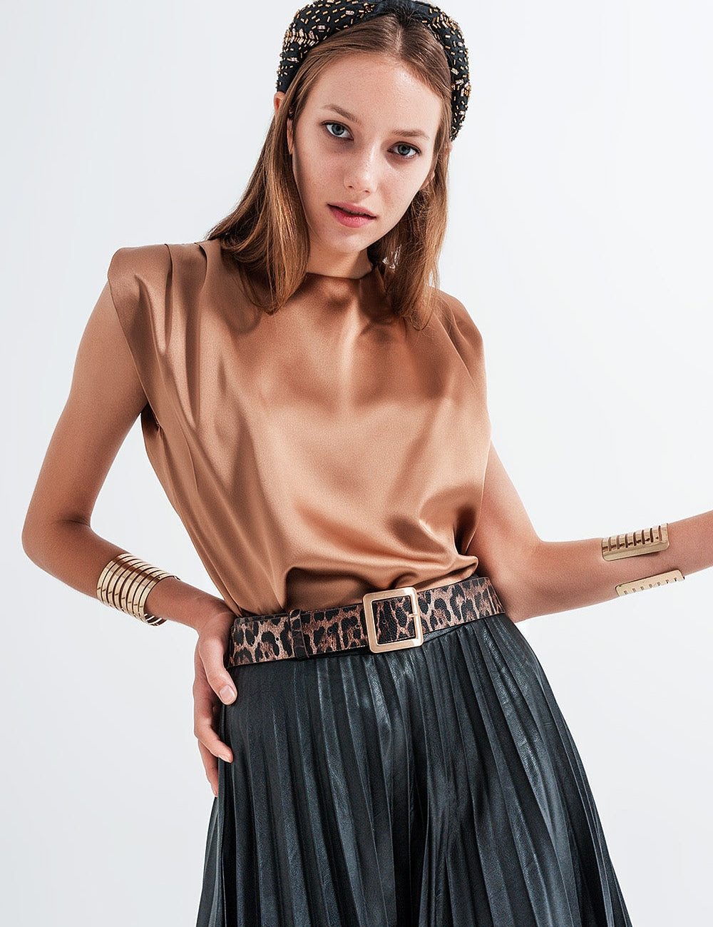 Model in Solene Satin Gold Shell with padded shoulders, crew neckline, and leopard print belt, showcasing elegant evening wear.