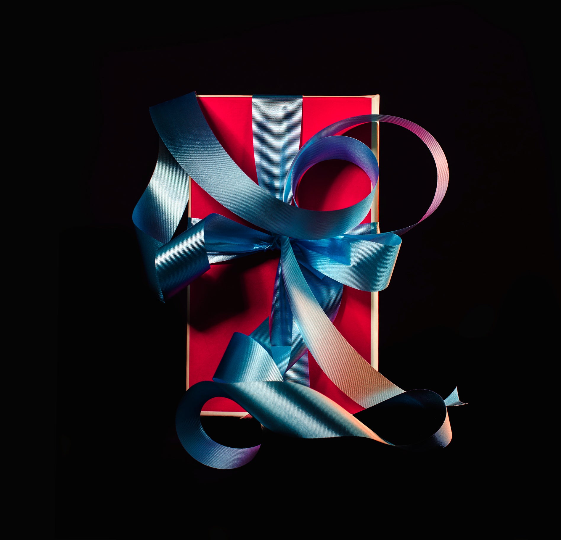 Red gift box with elegant blue ribbon bow on black background