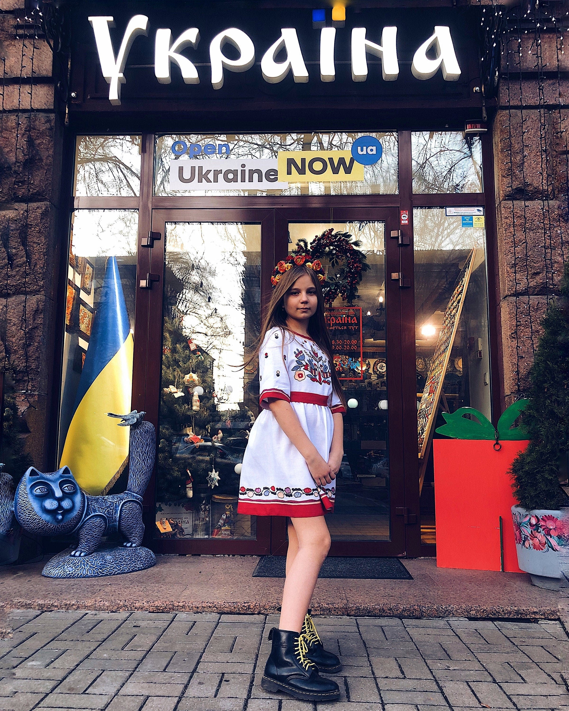 Girl in embroidered Ukrainian Vyshyvanka dress standing in front of a store with Ukraine themed decorations.