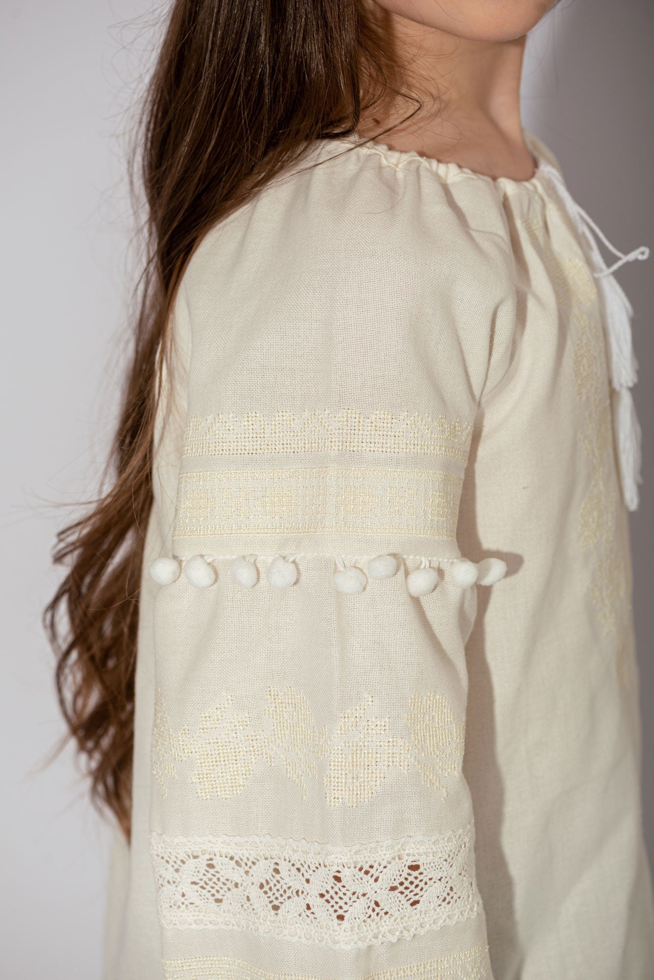 Girls’ vyshyvanka blouse with white embroidery and pom-poms, made from cotton linen blend, showcasing side view detail and craftsmanship.