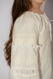 Girls’ vyshyvanka blouse with white embroidery and pom-poms, made from cotton linen blend, showcasing side view detail and craftsmanship.