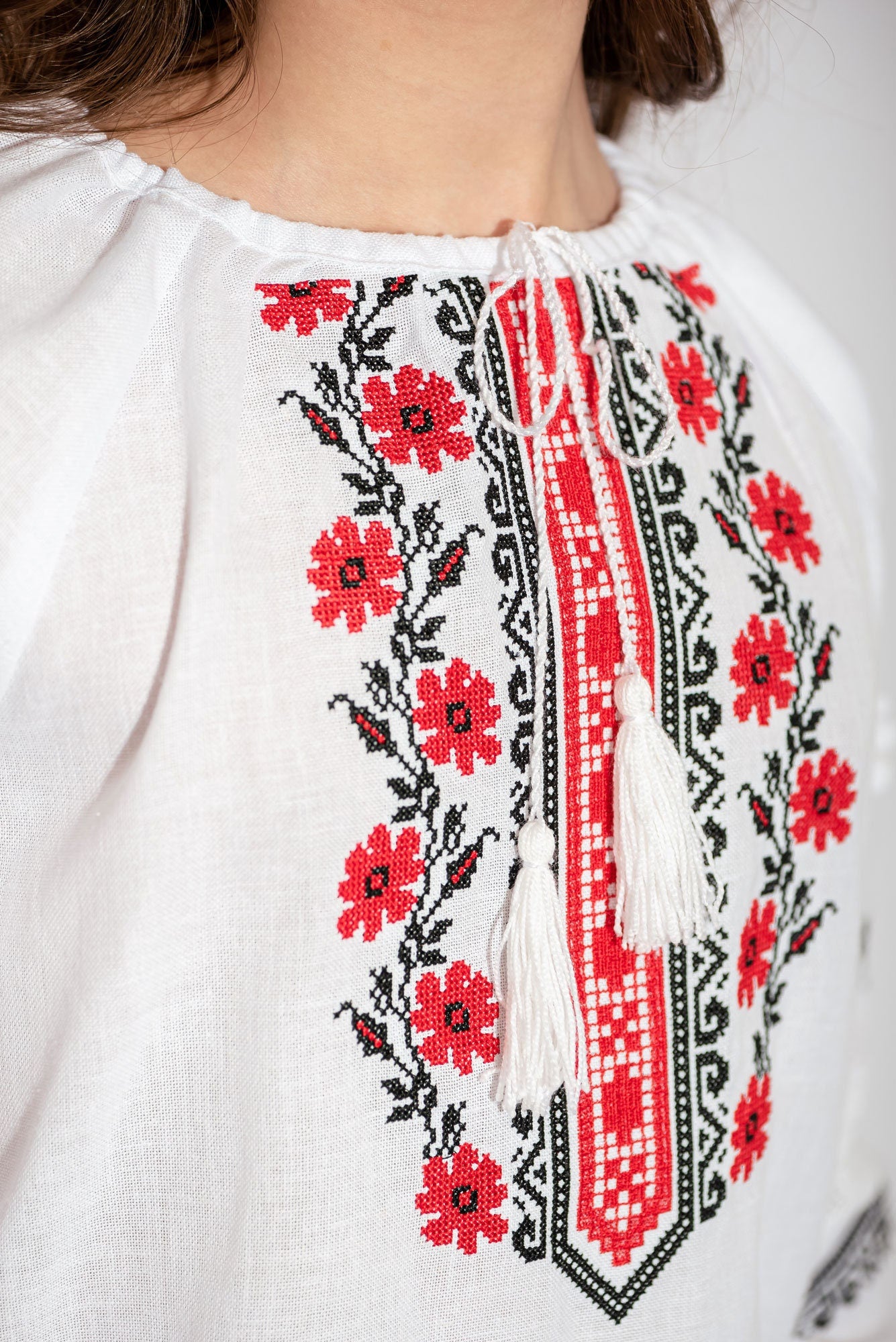 Close-up of girls' white vyshyvanka blouse with red and black floral embroidery, crafted in linen and cotton for traditional Ukrainian style.