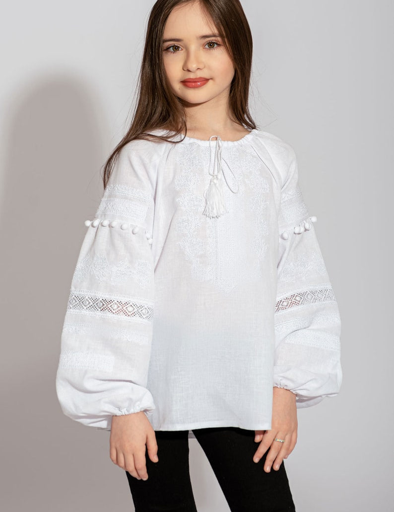Girl wearing embroidered white Ukrainian vyshyvanka blouse with red and black floral patterns, puff sleeves, and lace accents.