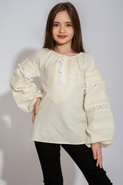 Girl wearing a white Vyshyvanka blouse with red and black floral embroidery, lace accents, and pom-poms. Traditional Ukrainian shirt.