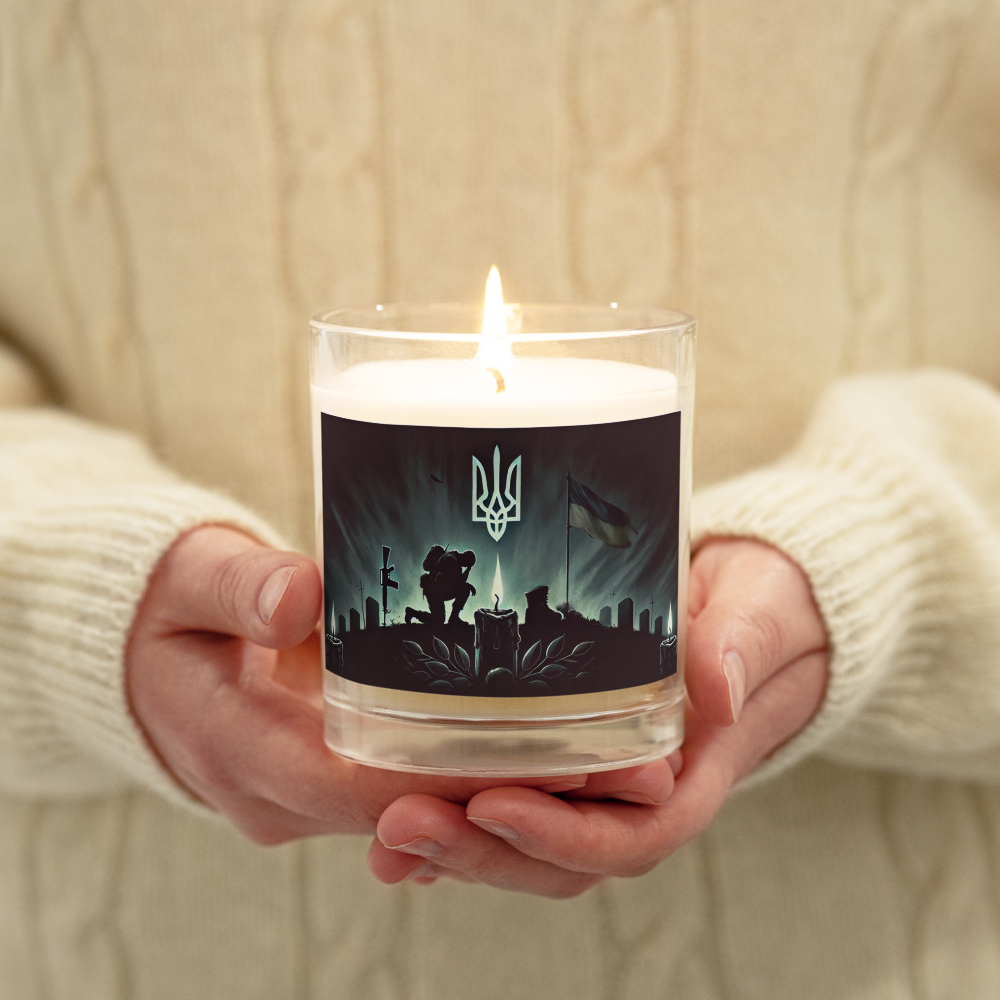 Hand holding lit soy wax candle with Ukrainian memorial design in glass jar, symbolizing reflection and patriotism.