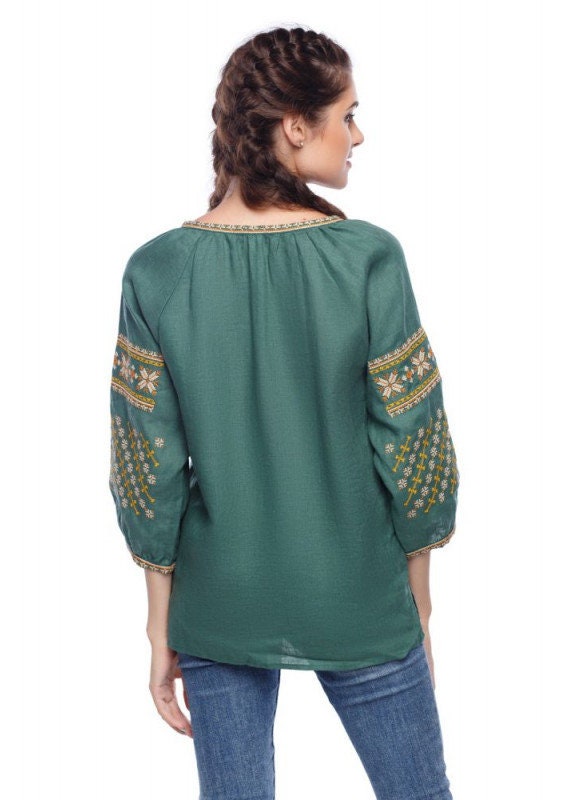 Woman wearing green Ukrainian embroidered linen blouse with Alatyr Star design, boho chic peasant style with ¾ raglan sleeves.