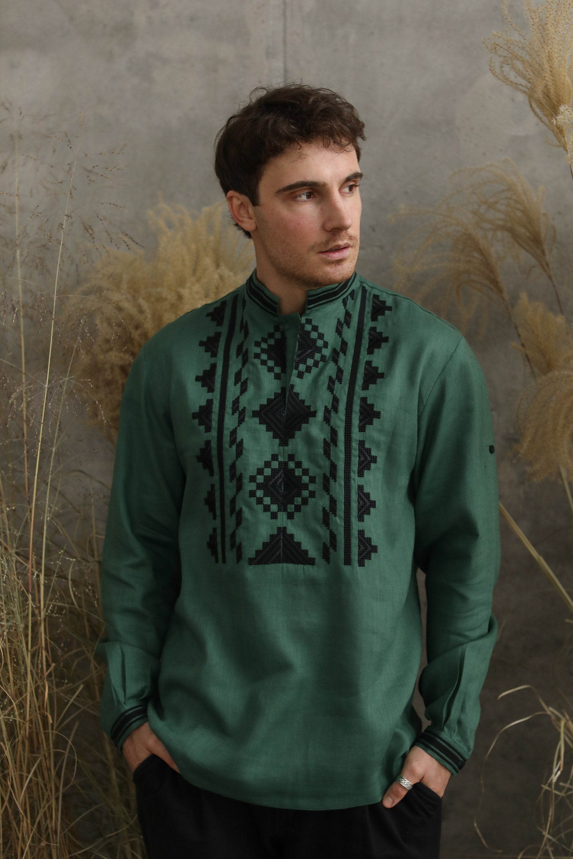 Green linen men's embroidered Ukrainian shirt with traditional black geometric patterns, modeled by a man against a neutral backdrop.