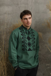 Green linen men's shirt with Ukrainian embroidery, vyshyvanka style, modeled against a textured wall.