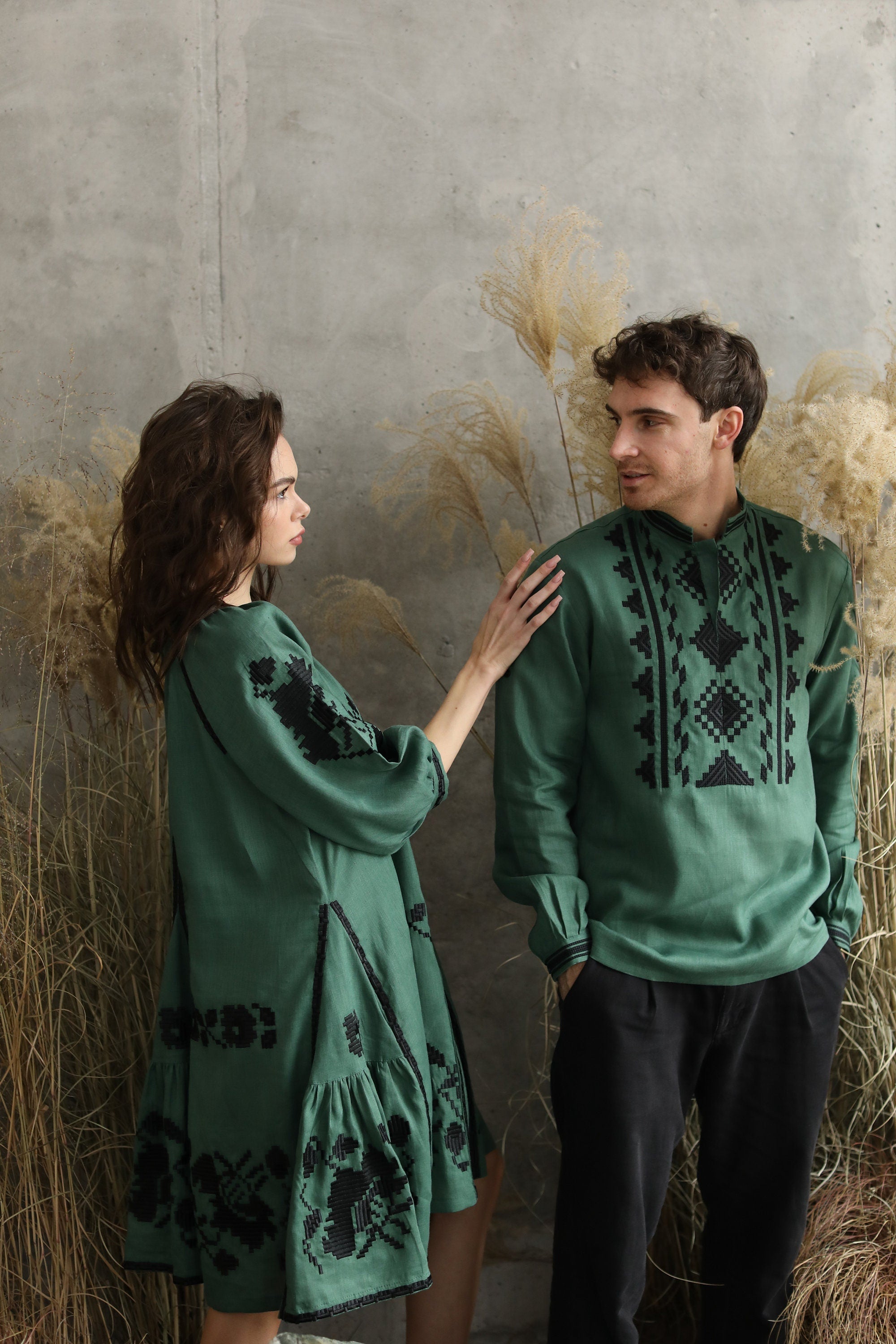 Couple wearing green linen embroidered Ukrainian shirts with black patterns, set against a rustic backdrop.
