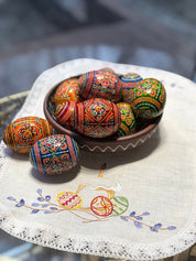 Set of hand-painted Ukrainian Easter wooden eggs with traditional pysanky designs in a bowl on an embroidered tablecloth
