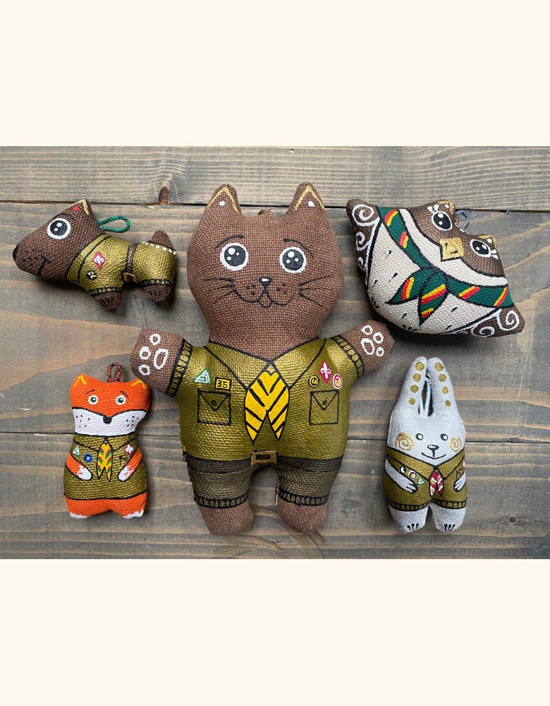 Hand-painted eco-friendly plush animals in scout uniforms, including a fox keychain, displayed on a wooden background as a souvenir.