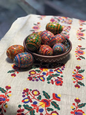 Hand-painted Ukrainian wooden Easter eggs in a bowl with intricate folk designs on a floral embroidered cloth.