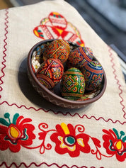 Bowl of six hand-painted Ukrainian pysanky eggs on embroidered cloth, showcasing traditional folk art and vibrant colors.