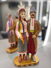 Hand-painted wooden couple figurine from Ukraine, depicting traditional folk attire, standing on a decorated base. Ideal wedding gift.
