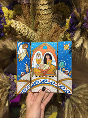 Hand holding a hand-painted wooden icon depicting a religious scene with vibrant colors, surrounded by dried flowers.