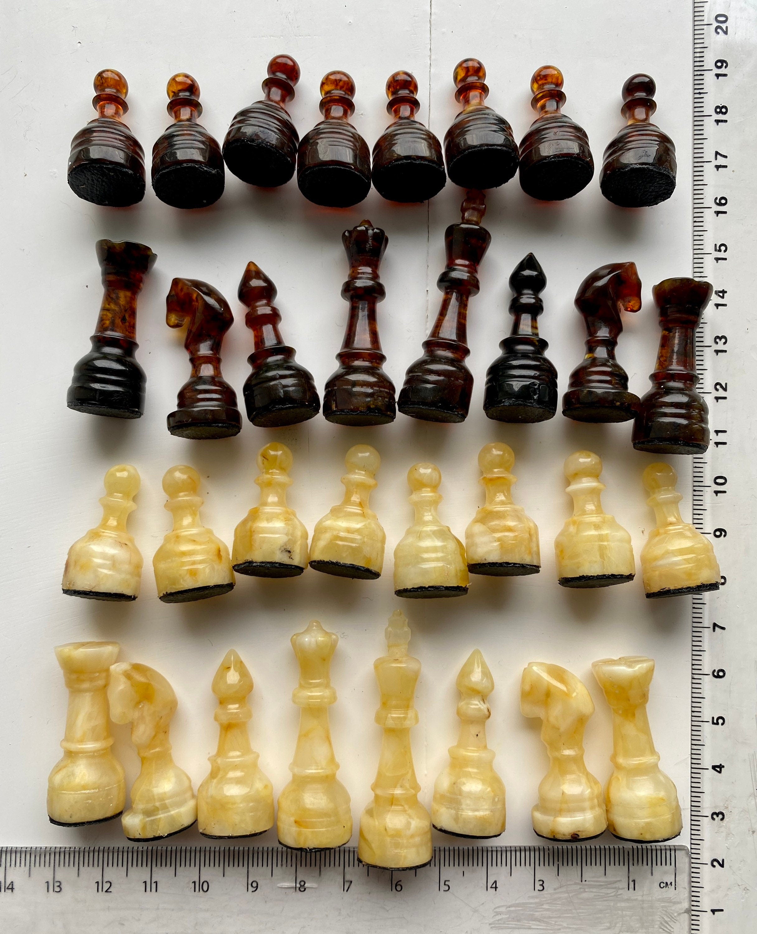 Handcrafted Baltic amber chess pieces in dark and light shades with a ruler for scale, perfect for collectors and enthusiasts.