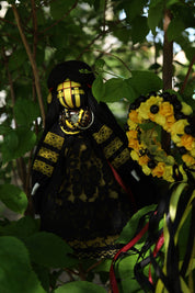 Handmade Ukrainian Motanka Doll with traditional black and yellow attire, nestled among green leaves, showcasing Slavic cultural heritage.