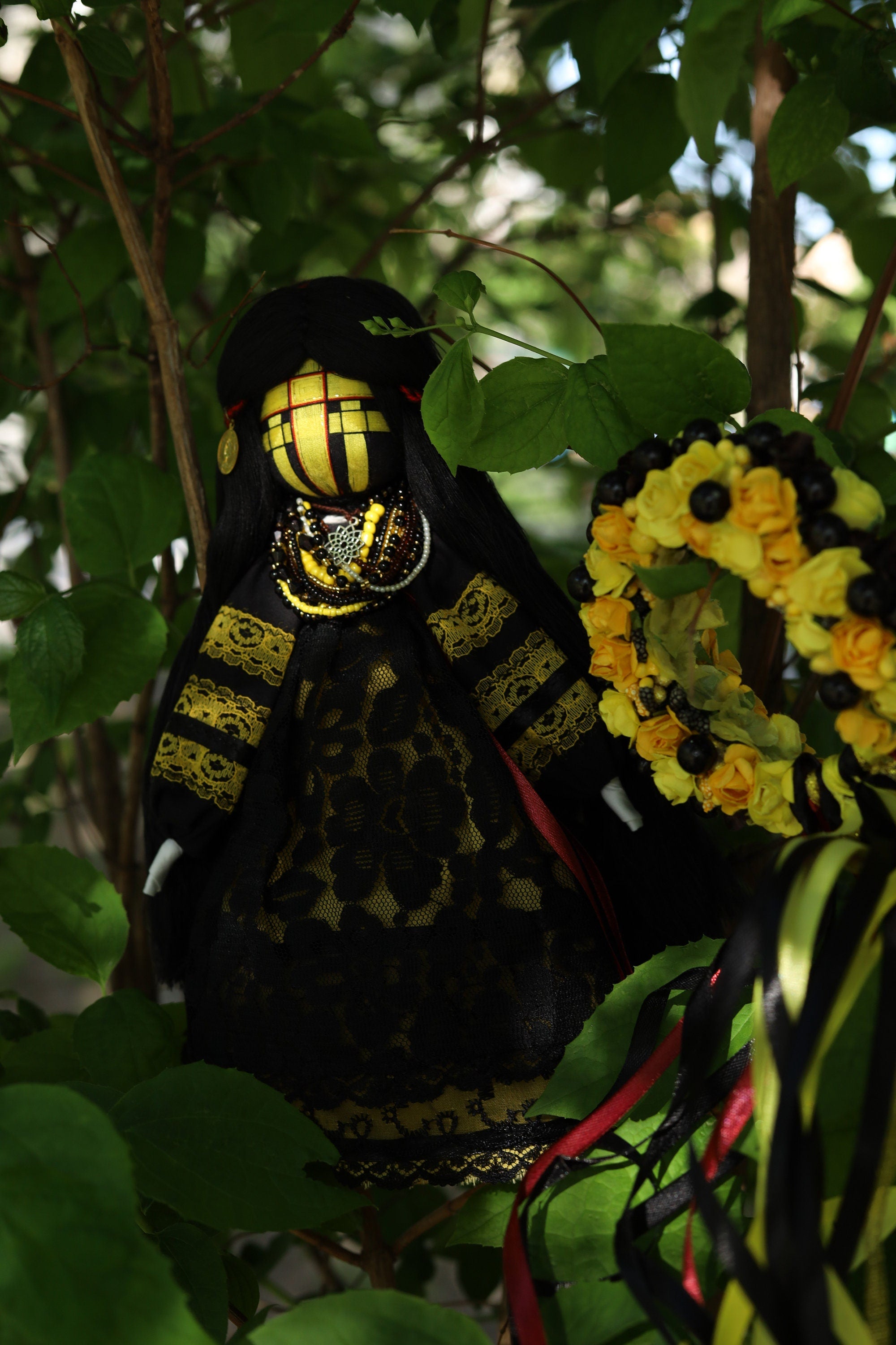 Handmade Ukrainian Motanka Doll with traditional black and yellow attire, nestled among green leaves, showcasing Slavic cultural heritage.
