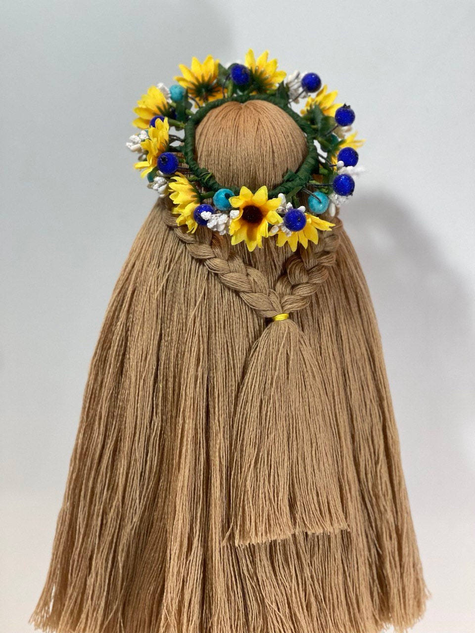 Handcrafted Ukrainian Motanka doll with floral headdress, symbolizing resilience and prosperity on wooden stand.