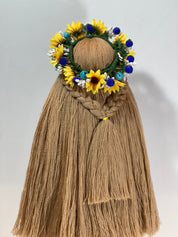 Handcrafted Ukrainian Motanka doll with floral headdress, symbolizing resilience and prosperity on wooden stand.