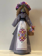 Handmade Ukrainian Bereginya Motanka doll on wooden stand with floral crown, embroidered dress, and basket, symbolizing protection.