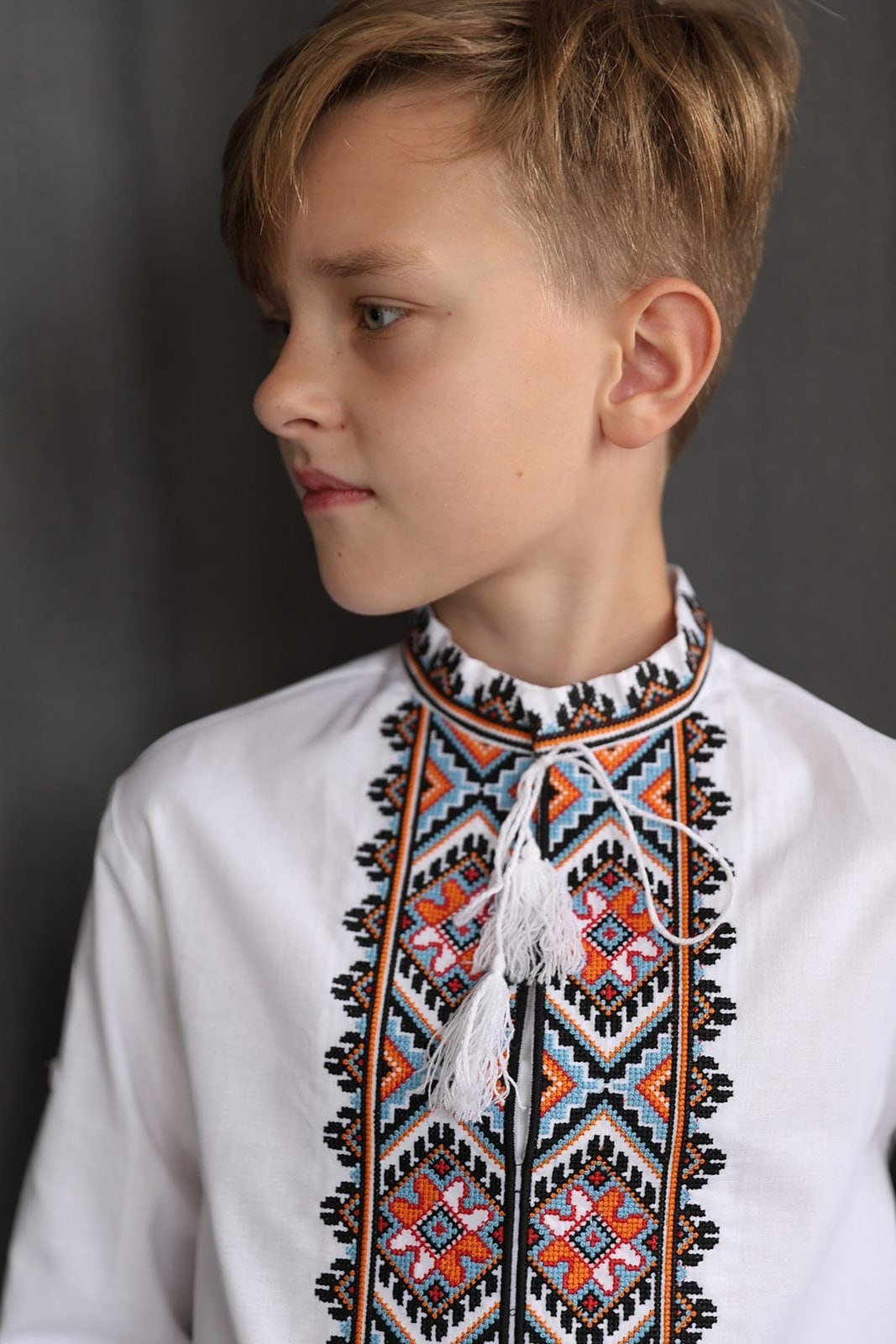 Boy wearing handmade Ukrainian Vyshyvanka, a white cotton shirt with traditional embroidered cross-stitch design.