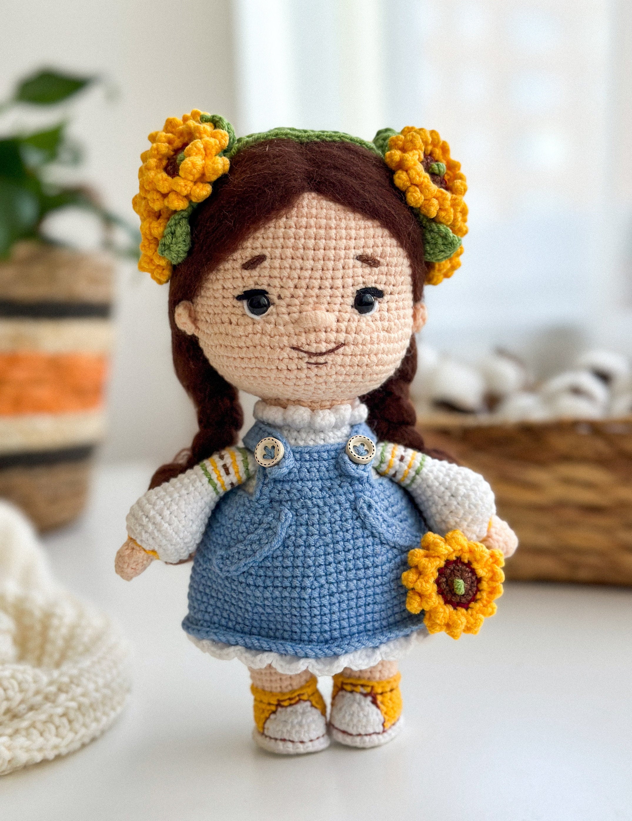 Handmade knitted doll with sunflower decorations, wearing a blue dress, on a cozy indoor background. Perfect Ukrainian-themed gift.