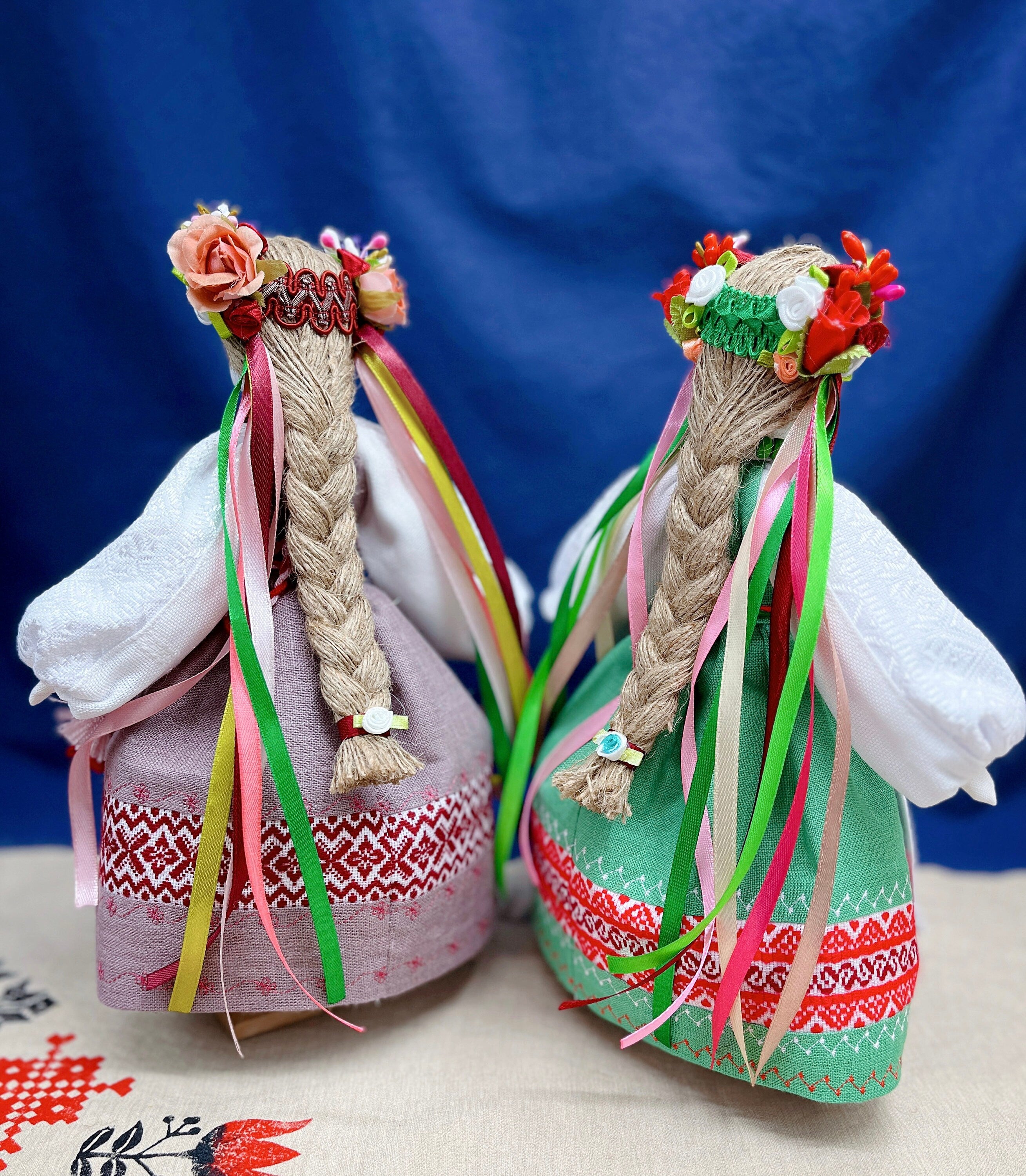 Handmade Motanka dolls in traditional Ukrainian attire, featuring colorful ribbons and floral crowns against a blue background.