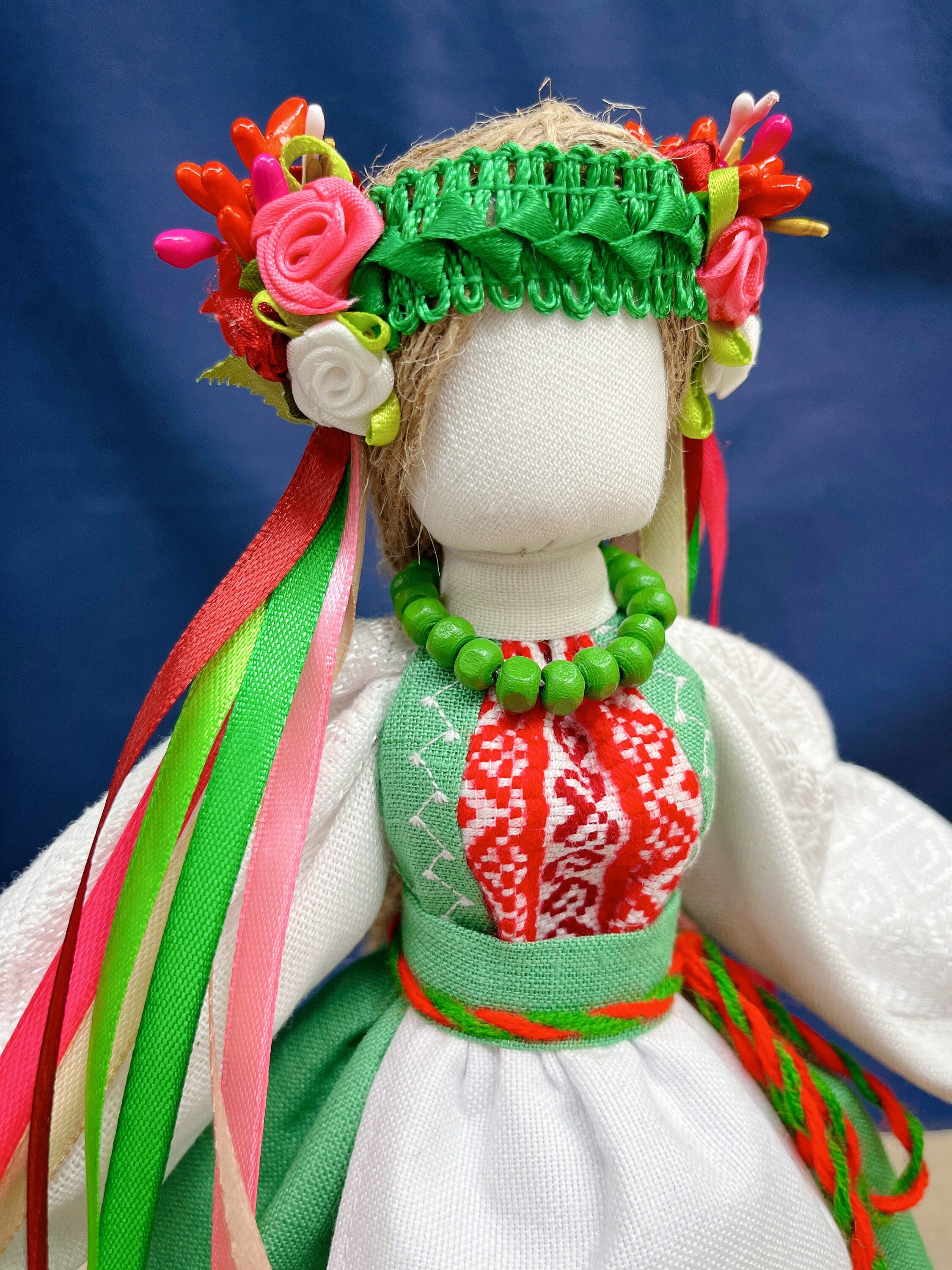 Handmade Motanka doll in vibrant Ukrainian attire with floral headdress and beaded necklace, symbolizing prosperity and protection.