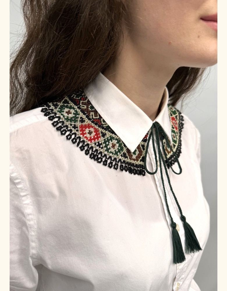 Woman wearing handmade Ukrainian Kryza necklace with green, beige, and red beaded vyshyvanka collar on a white shirt.