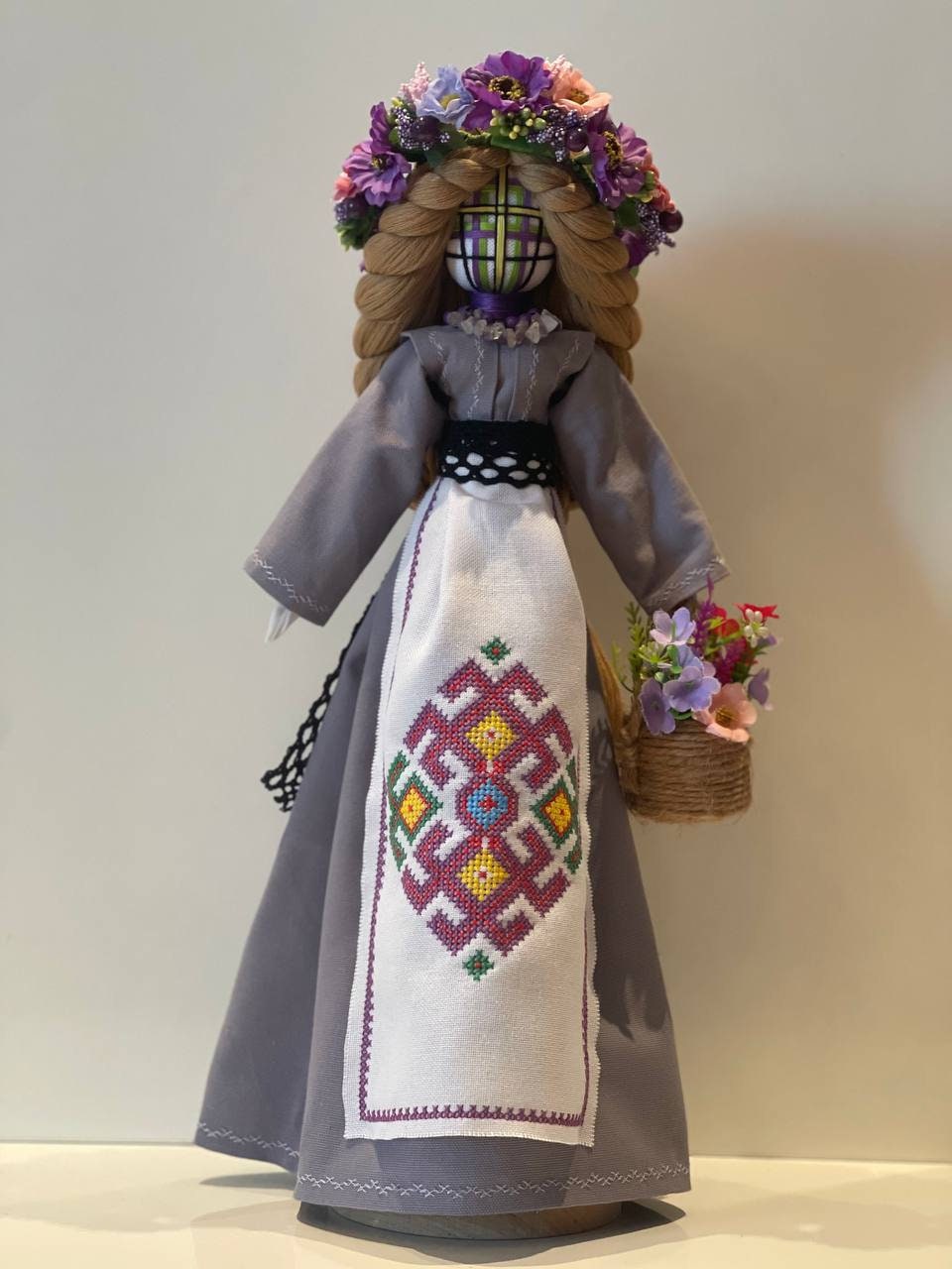 Handmade Ukrainian Motanka Bereginya doll with floral headpiece and embroidered dress on wooden stand, symbolizing protection and prosperity.