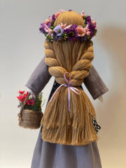 Handmade Ukrainian Bereginya Motanka doll with braided hair, purple floral crown, and basket on a wooden stand. Folk art gift for Easter.