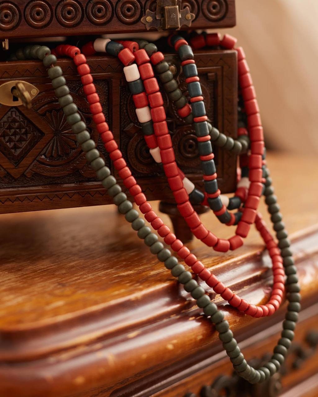 Handmade Ukrainian necklace with red and green ceramic beads, draped over an ornate wooden chest, showcasing ethnic elegance.