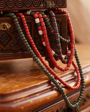 Handmade Ukrainian necklace with red and green ceramic beads, draped over an ornate wooden chest, showcasing ethnic elegance.