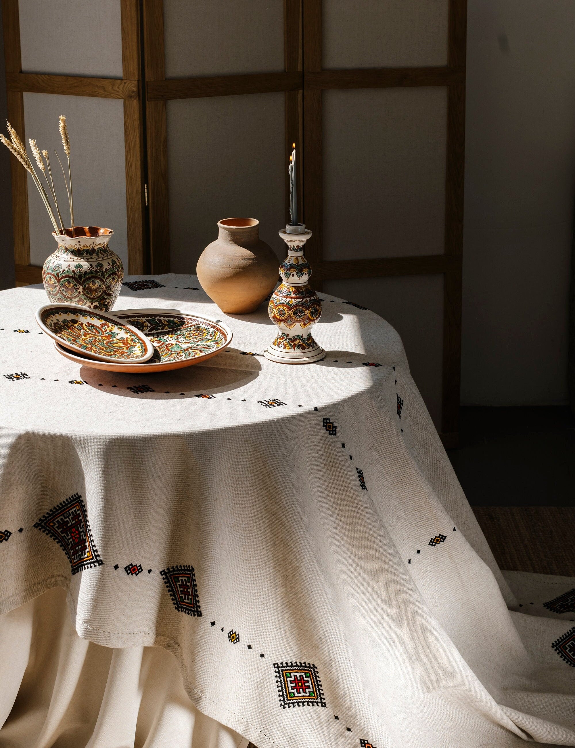 Handmade Ukrainian embroidered tablecloth with traditional ethnic designs, set on a dining table with decorative pottery.