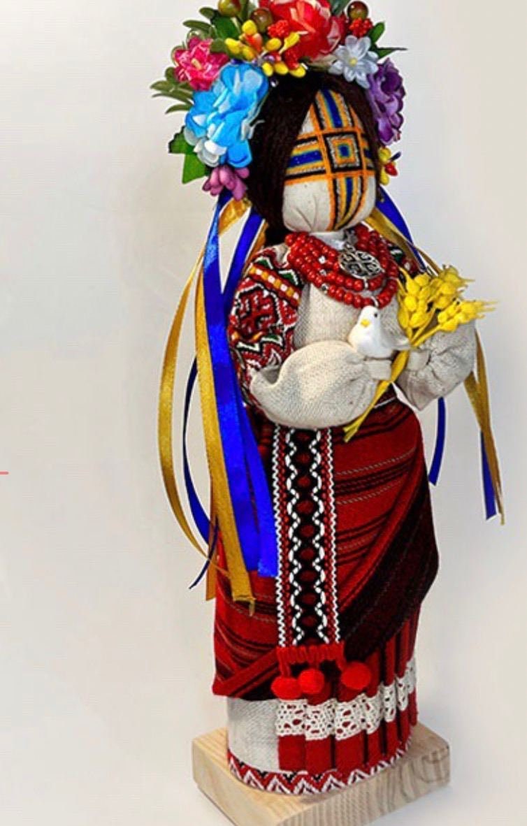 Unique handmade Ukrainian Motanka Doll "Invincible" with dove and wheat, symbolizing strength and peace, on a wooden stand.