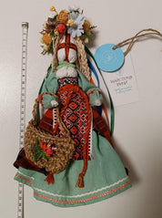 Traditional Ukrainian Motanka doll with colorful dress and floral headpiece, standing beside a measuring tape.